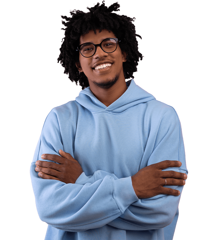 A cheerful young man with glasses and curly hair wearing a light blue hoodie stands with arms crossed, smiling confidently.