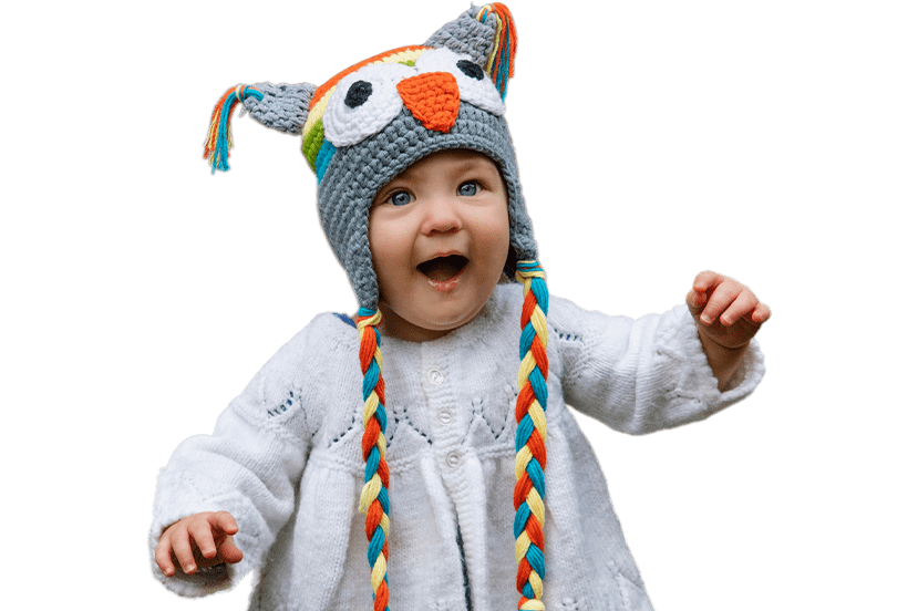 A joyful baby wearing a colorful owl hat and a white sweater, with an excited expression