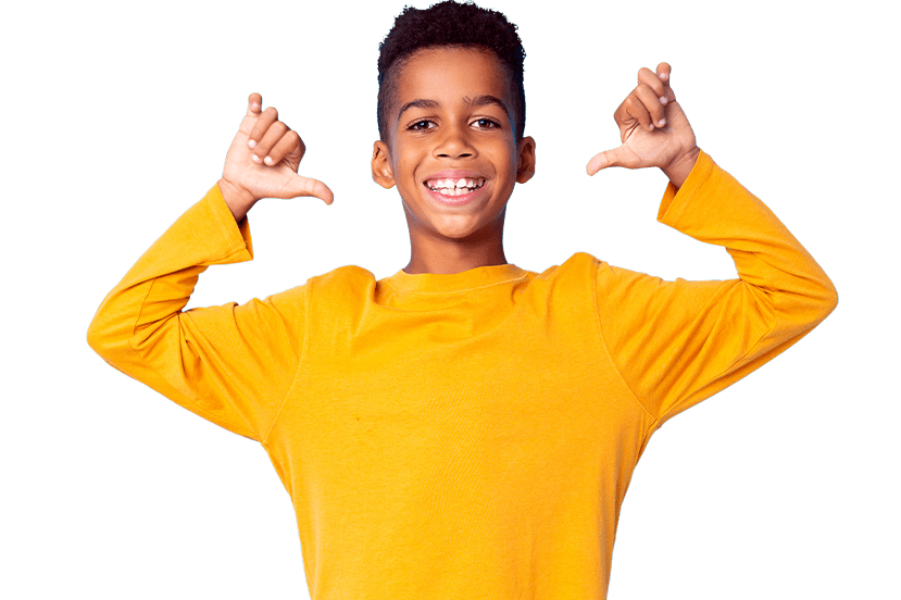 A cheerful young boy with short curly hair, wearing a yellow long-sleeve shirt, smiling and playfully gesturing thumbs up with both hands