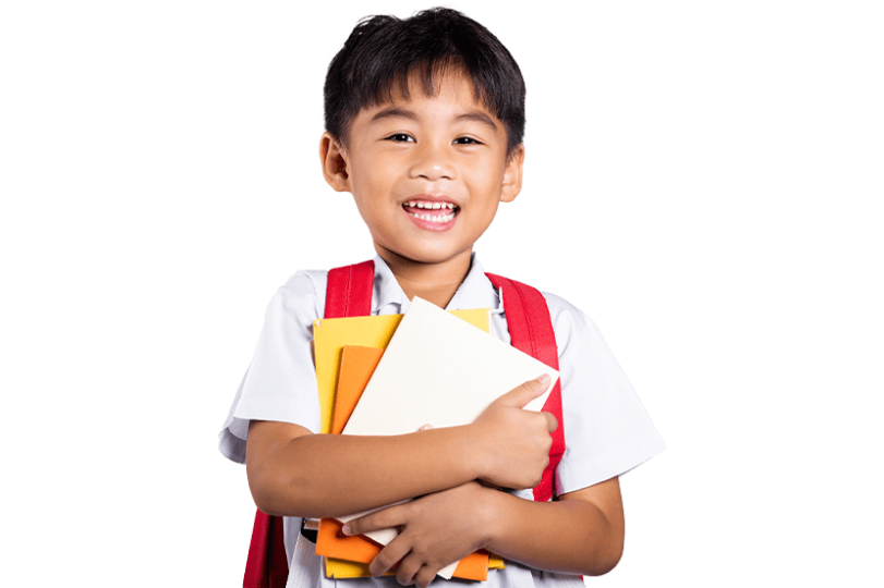 A young boy with a big smile, wearing a white shirt and red suspenders, holds a stack of colorful books. He carries a white backpack, filled with materials for his studies