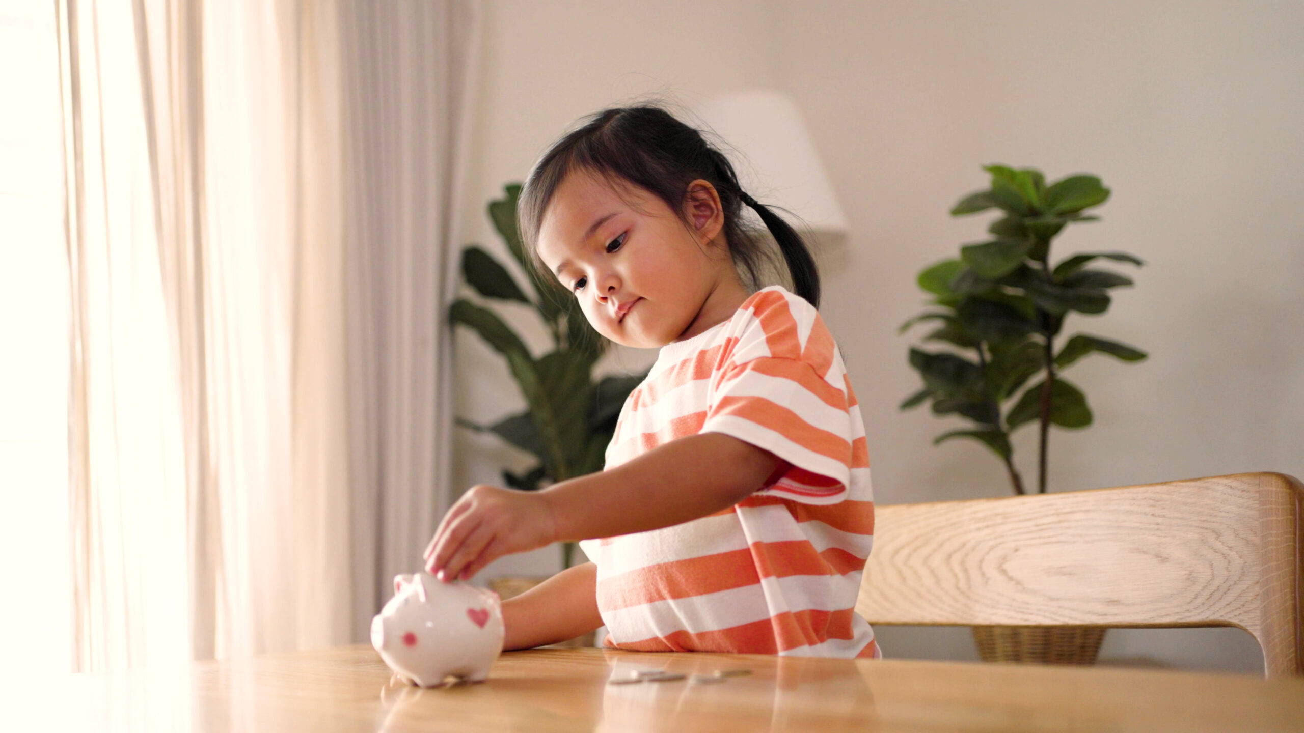 Young girl putting coins into a piggy bank