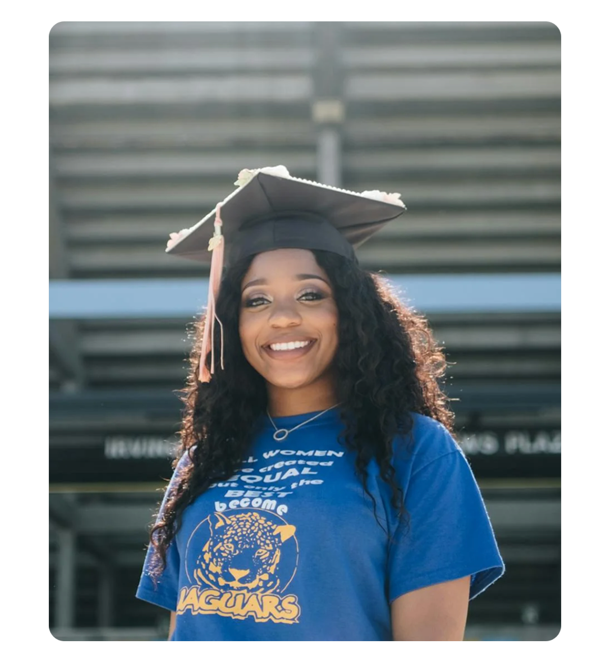 A young woman in a blue graduation cap and gown smiles proudly, celebrating her academic achievement.