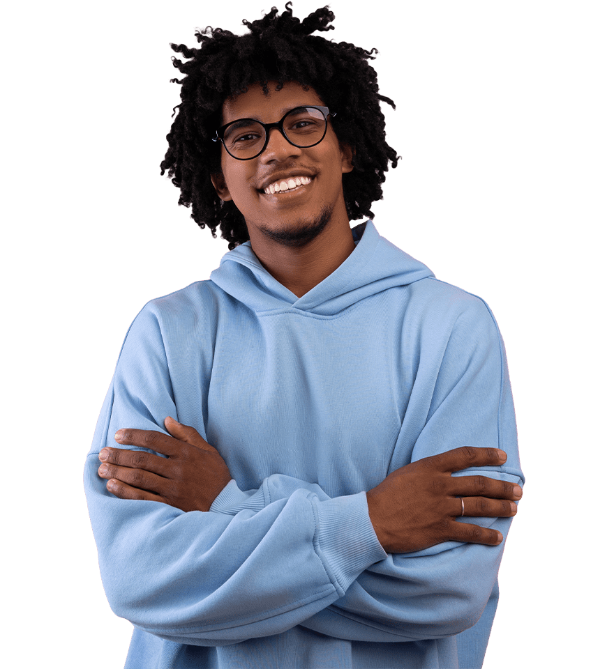 A cheerful young man with glasses and curly hair wearing a light blue hoodie stands with arms crossed, smiling confidently.