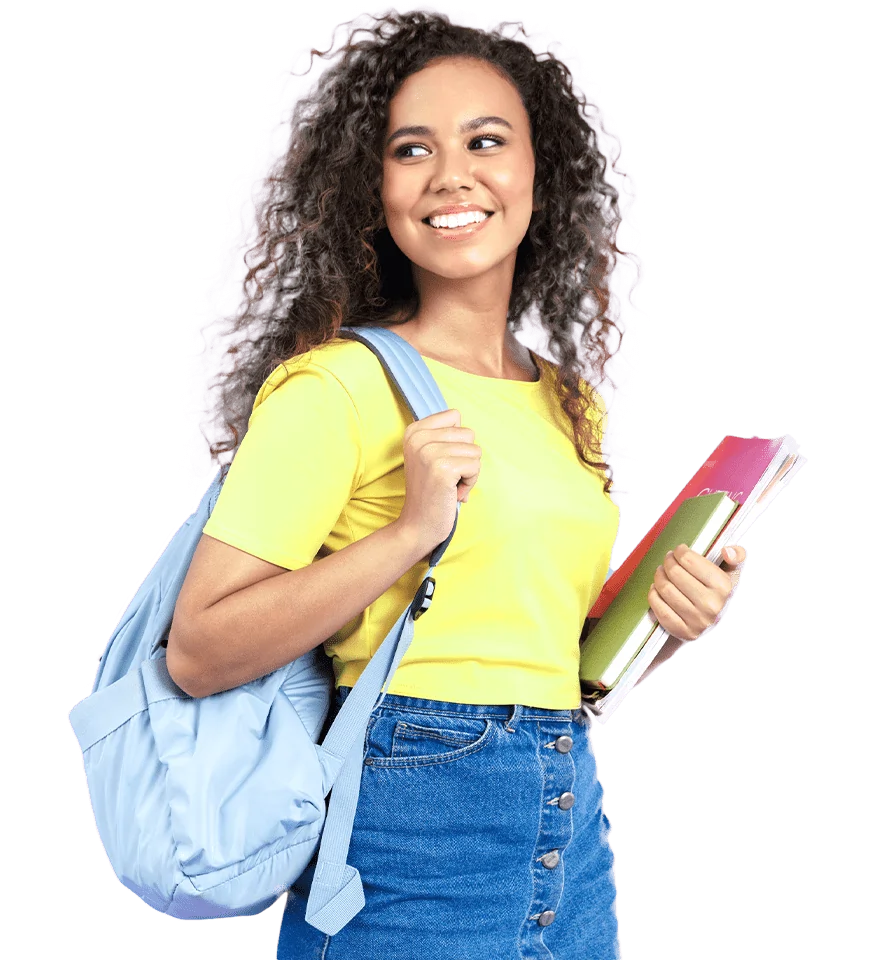 A young woman with curly hair smiles while holding textbooks and wearing a yellow t-shirt and denim jeans, carrying a blue backpack over one shoulder as she heads to her post-secondary education classes.