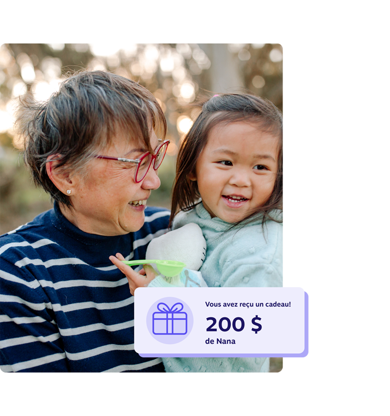 Une grand-mère souriante tenant sa petite-fille à l’extérieur, avec une notification indiquant un cadeau REEE de 200 $ de la part de grand-maman.