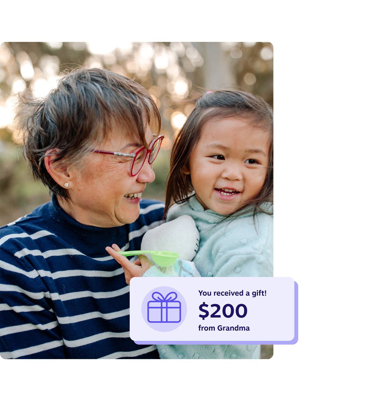 Smiling grandmother holding her young granddaughter outdoors, with a notification showing a $200 RESP gift from Grandma.