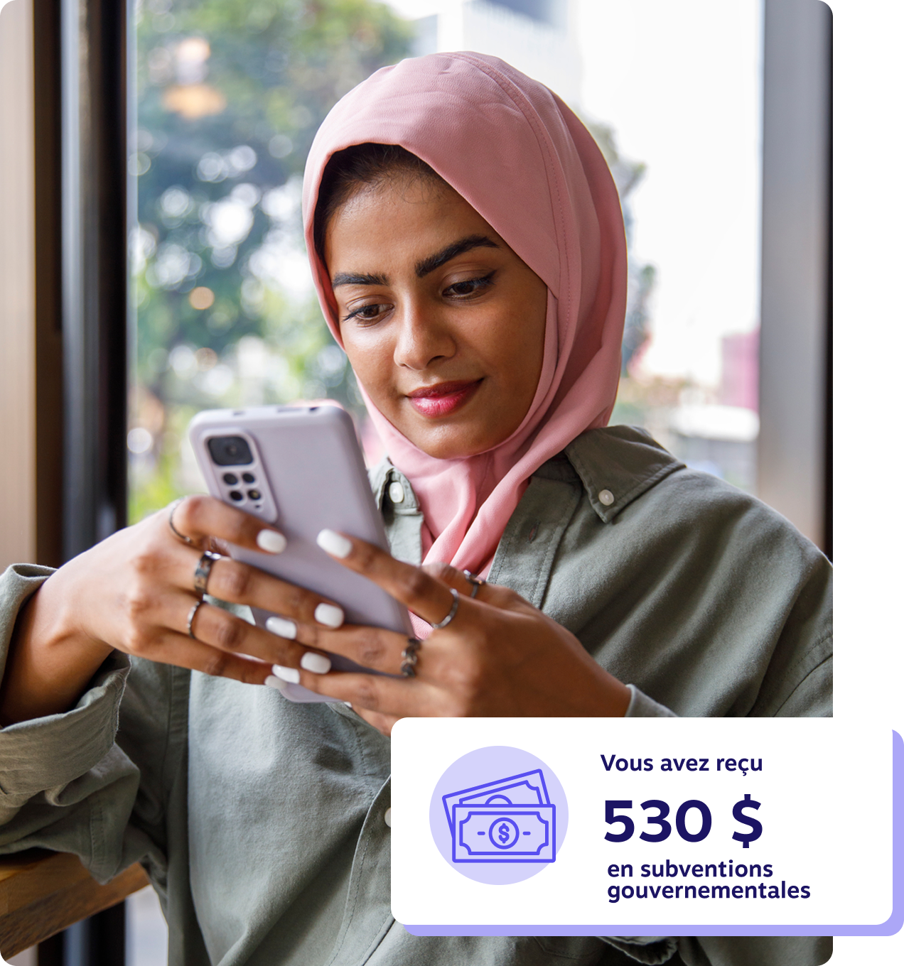 Jeune femme portant un hijab rose regardant son téléphone près de la fenêtre d’un café, avec une notification indiquant qu’elle a reçu 530 $ en subventions gouvernementales.