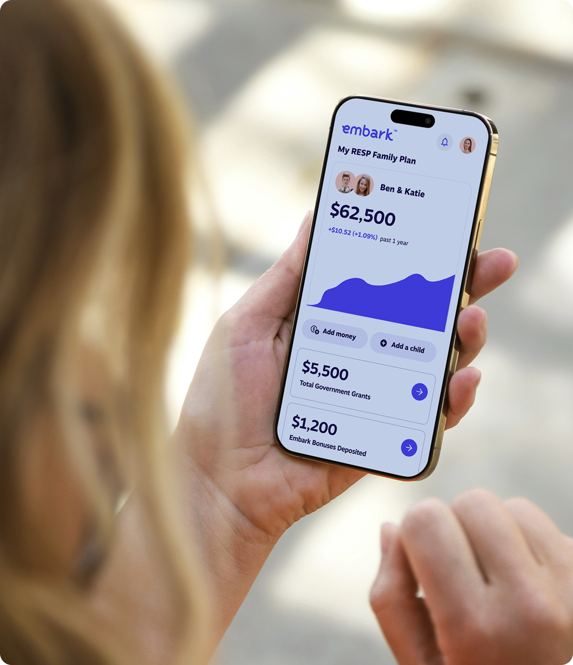 Close-up of a woman holding a smartphone displaying the Embark RESP app, showing savings progress for two children.
