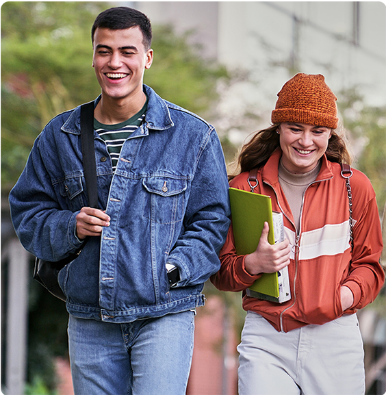 Two smiling students walking outdoors on campus, carrying school supplies and chatting.