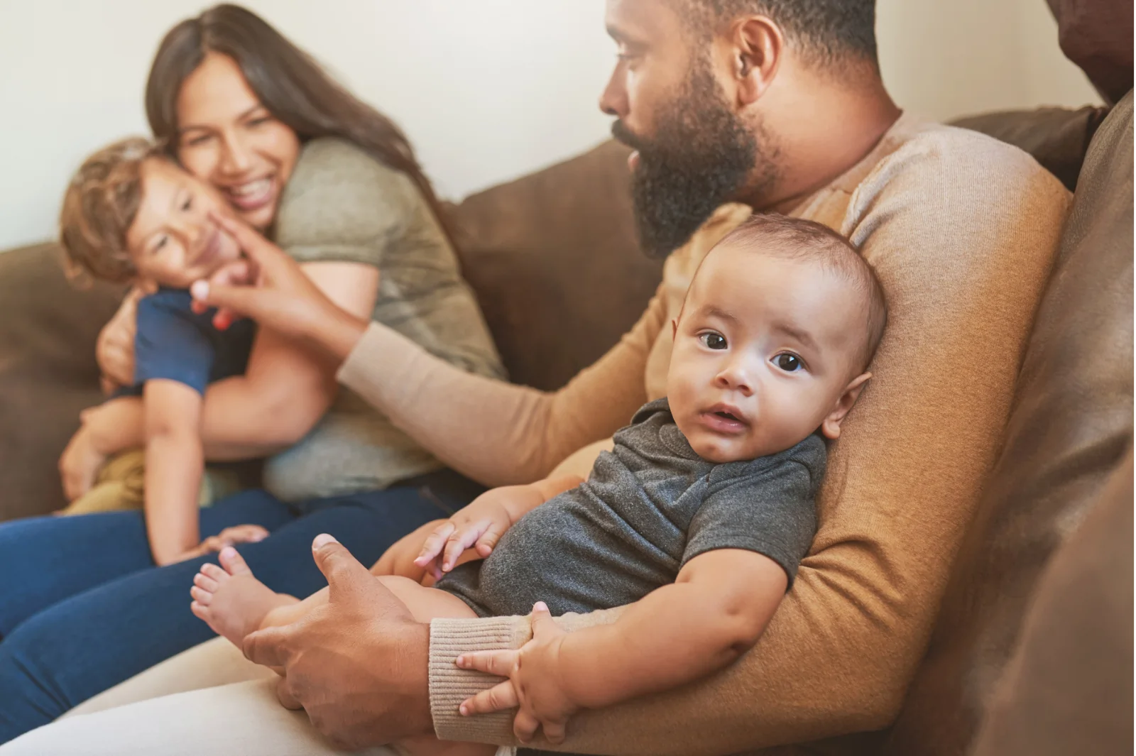 Father sitting with baby while reaching to older child who is sitting and laughing with their mom