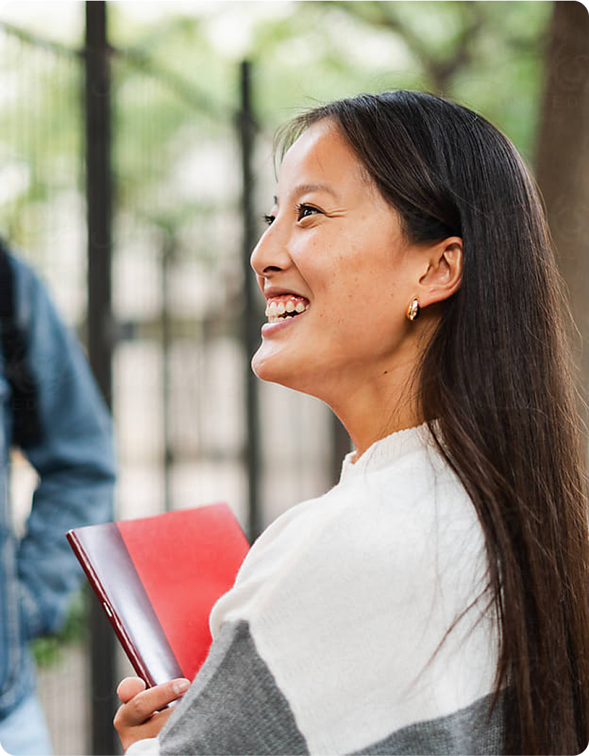 A woman beams with a smile while holding a bright red folder in her hands.