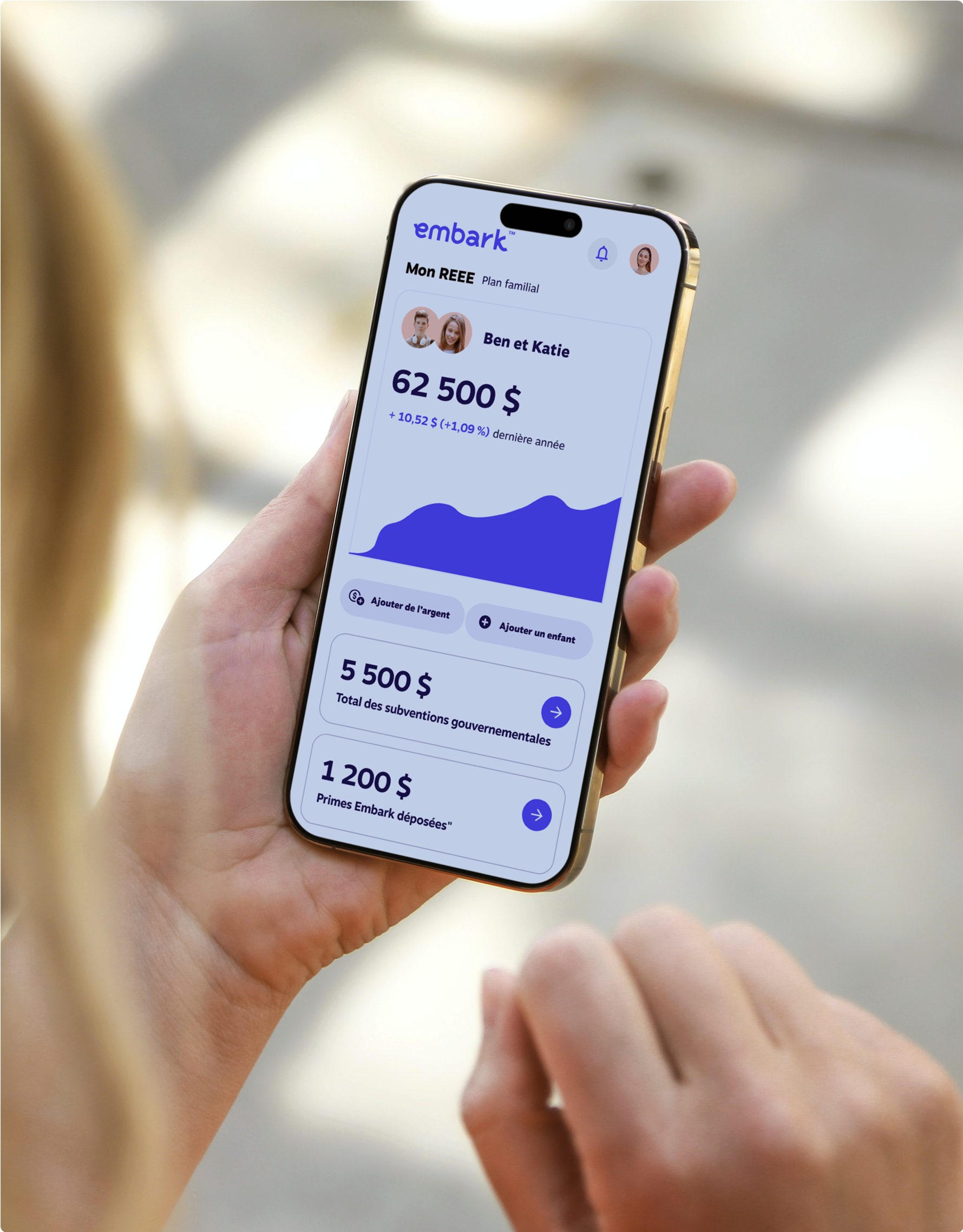 Gros plan d’une femme tenant un téléphone intelligent affichant l’application REEE d’Embark, montrant l’épargne accumulée pour deux enfants.