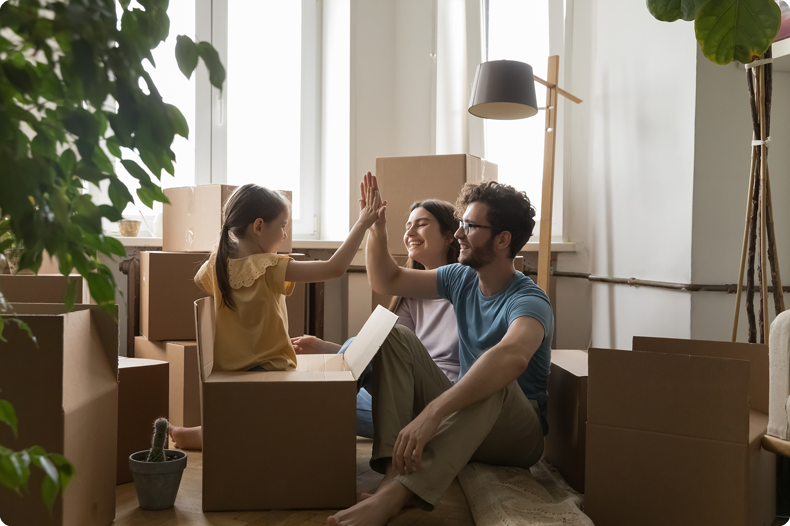 Parents packing boxes with child playing in box giving them a high-five smiling.