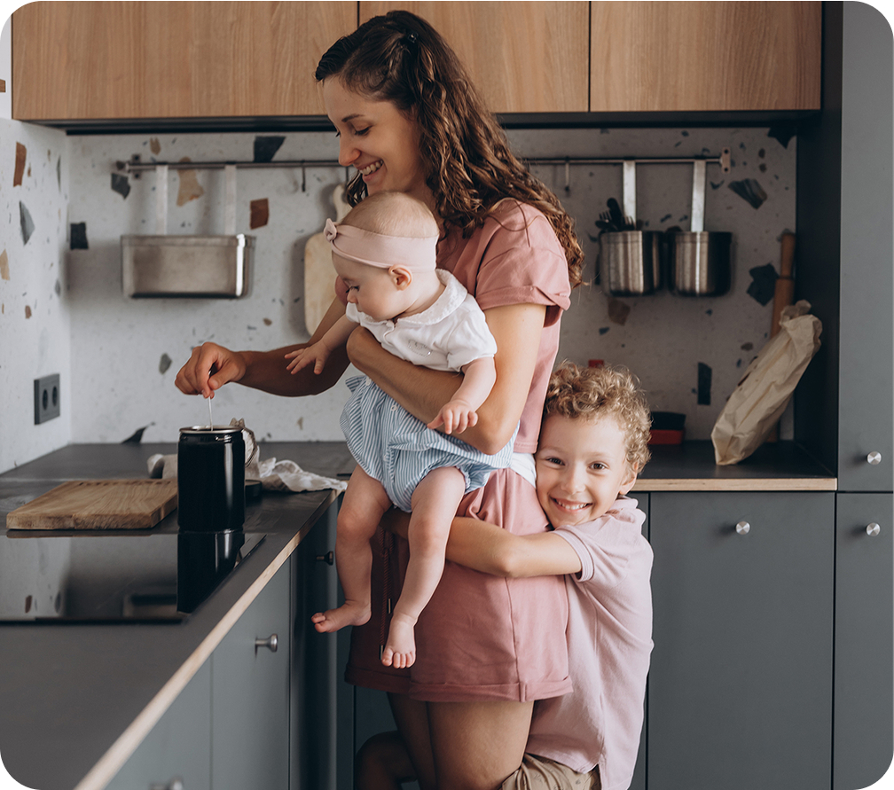 A woman and two children happily cooking together in a bright, cheerful kitchen.