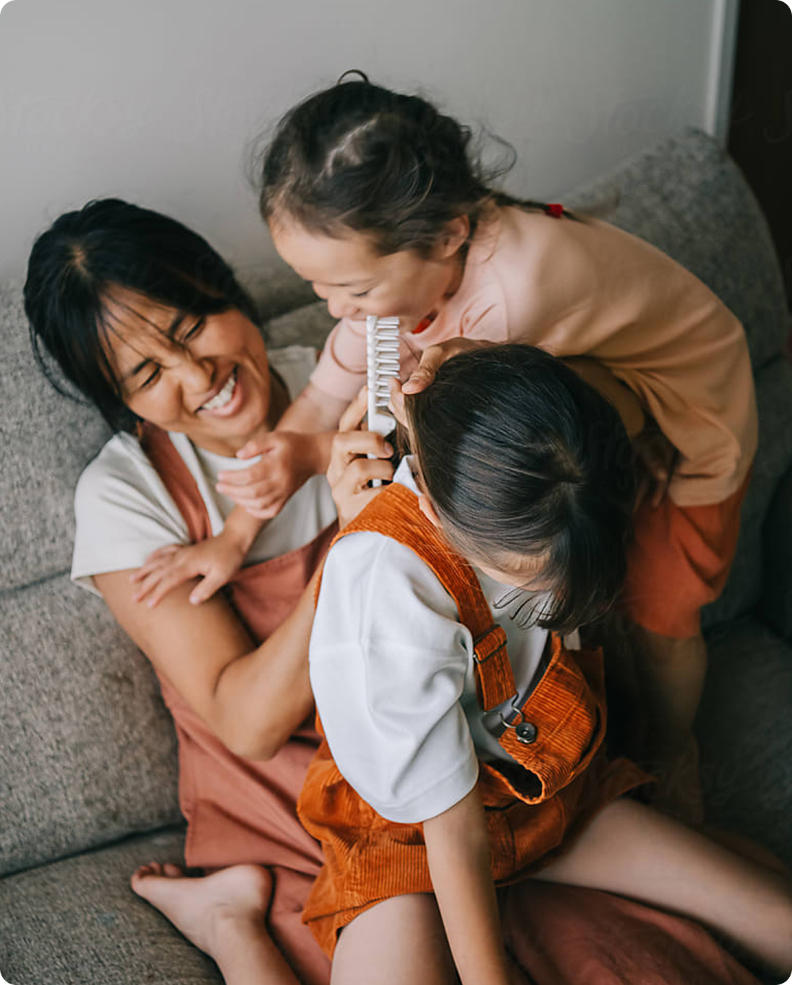 A mother and two children are sitting together on a couch, smiling and enjoying each other's company.