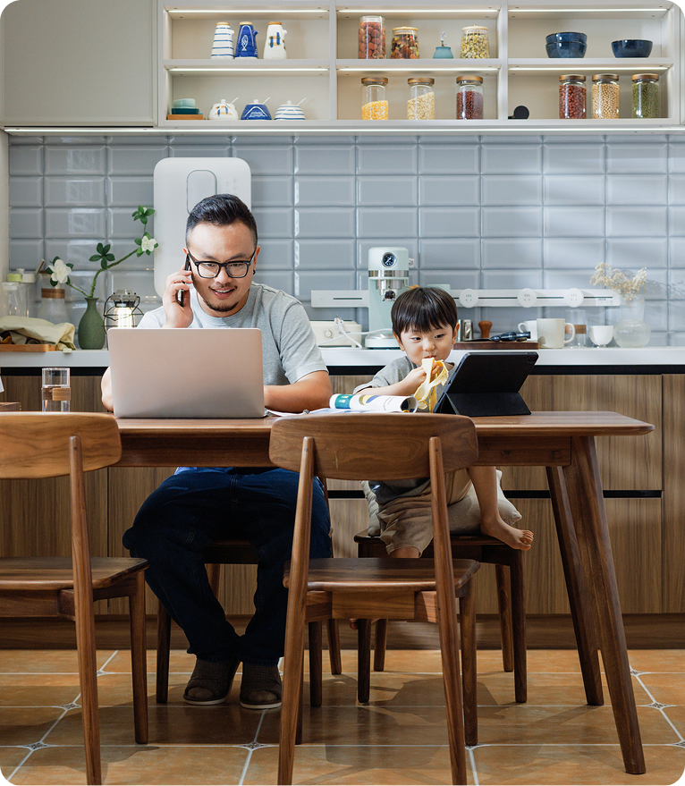 A man and a child sit together at a table, focused on a laptop screen, sharing a moment of learning or play.
