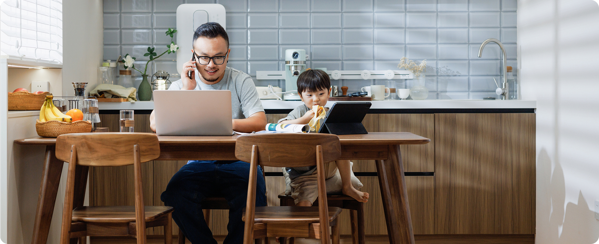 A man and a child sit together at a table, focused on a laptop screen, sharing a moment of learning or play.