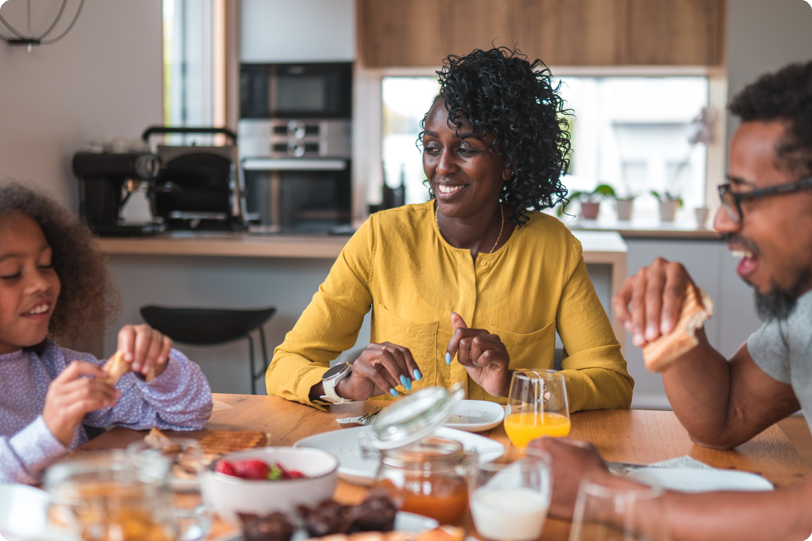 Woman in yellow shirt smiling while eating breakfast with her family at kitchen table