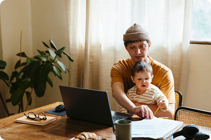 A man and a baby sit together at a table, focused on a laptop in front of them.